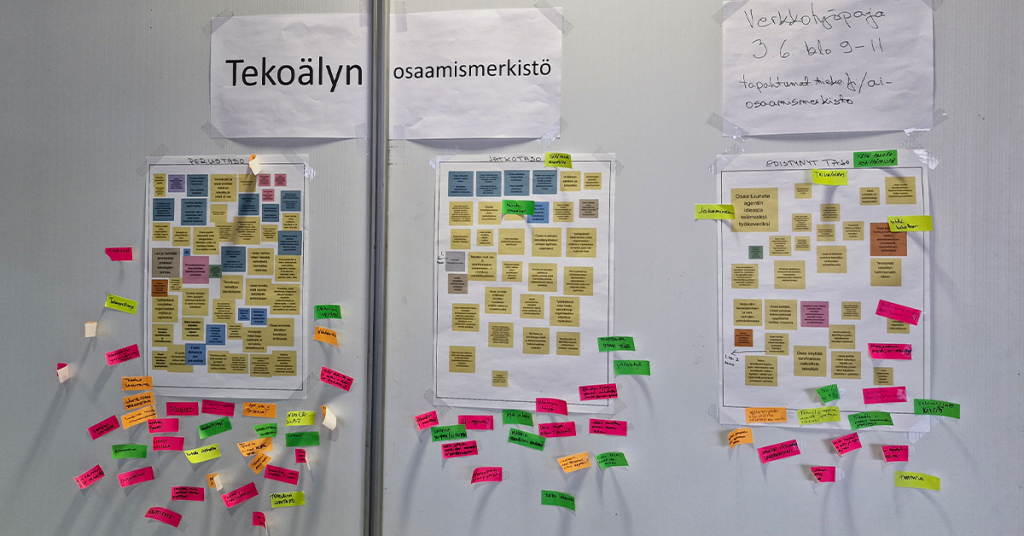 Seinälle on teipattu kolme suurta paperia, joihin on kiinnitetty runsaasti erivärisiä muistilappuja. Yhdessä ne muodostavat ryhmiteltyjä kokonaisuuksia. Laput sisältävät käsinkirjoitettuja muistiinpanoja ja ideoita. Paperien ympärille on lisätty lisää värikkäitä muistilappuja, jotka täydentävät sisältöjä. Kokonaisuus viestii työpajassa syntyneestä yhteisestä ideoinnista ja jäsentelystä.